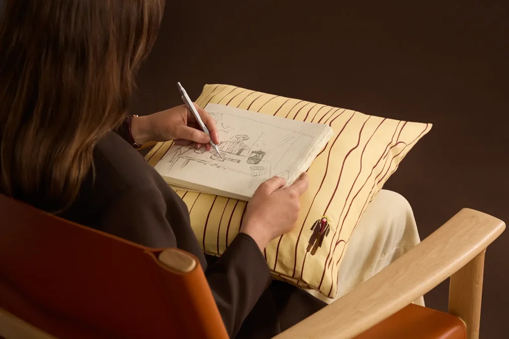 Justine Franco dibujando en su cuaderno, apoyado sobre un cojín de rayas de su colección de cerámica y textiles para Kave.